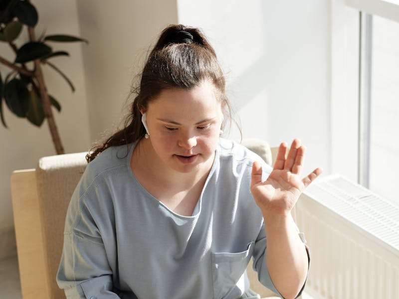 Woman in a Blue Top Using a Laptop Near a Glass Window